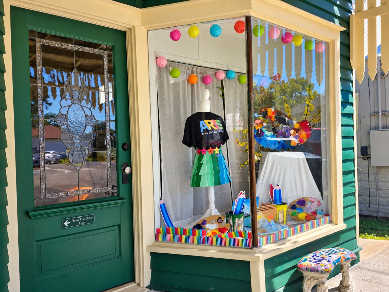 Art-themed window display beside a green door in Fayetteville